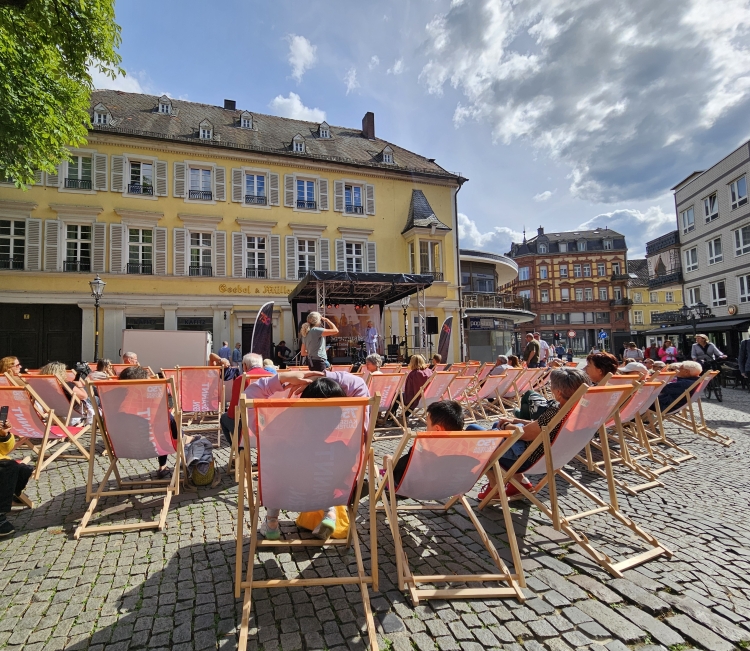 Blick über die Liegestühle auf die Bühne am Martinsplatz, wo Beate Kimmel gerade am Mikrofon steht © Stadt Kaiserslautern
