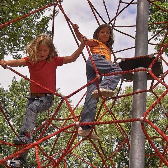 Zwei Mädchen klettern in dem mit roten Seilen bespannten Klettergerüst. 