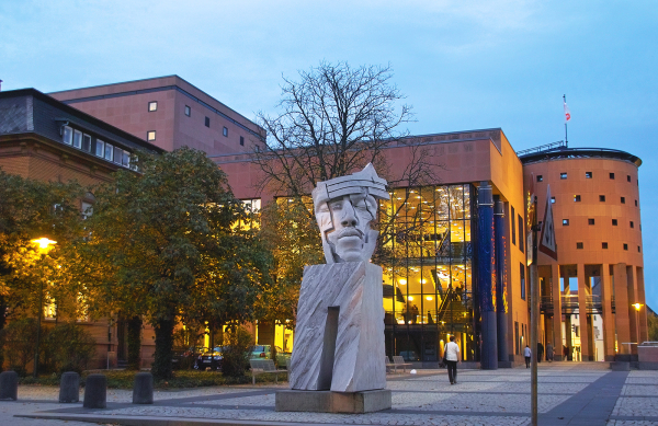 das beleuchtete Pfalztheater mit Plastik im Vordergrund in der Abenddämmerung
