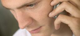 Ein junger Mann telefoniert mit seinem Handy. Sein Kopf neigt er dabei nach vorne