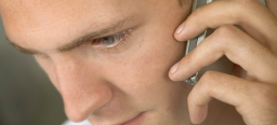 Ein junger Mann telefoniert mit seinem Handy. Sein Kopf neigt er dabei nach vorne