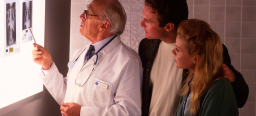Ein Arzt zeigt einem jungem Paar Röntgenbilder. Er zeigt auf den Bauchbereich.