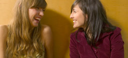 zwei lachende Frauen sitzen nebeneinander und schauen sich an
