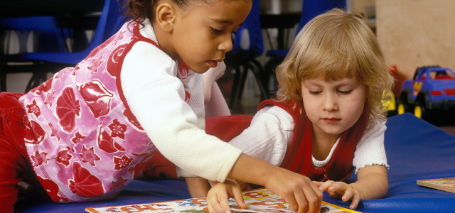 Zwei Mädchen spielen mit einem Zahlenpuzzle. Im Hintergrund sind Stühle, eine Tafel und ein Spielzeugauto zu erkennen.     
