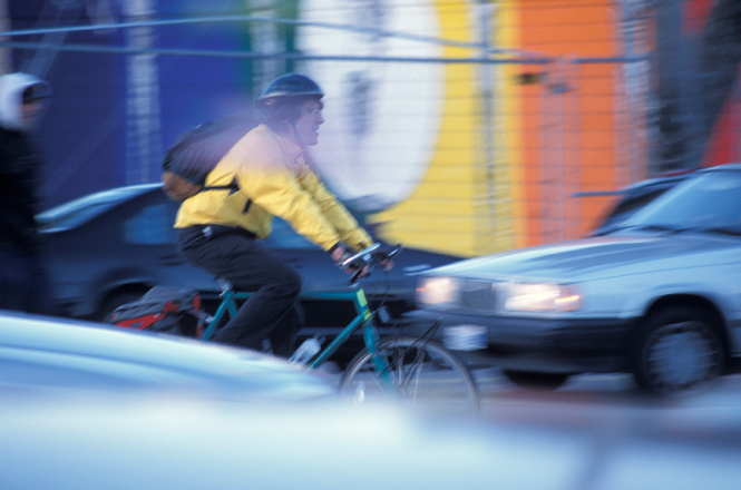 Ein Mann fährt mit einem grünen Fahrrad auf ein stark befahrenen Straße  