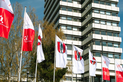 wehende Fahnen vor dem Kaiserslauterer Rathaus  - Hochformatfahnen 4 mit Kaiserslauterer Wappen auf weißem Grund; 4 Fahnen zweigeteilt: rotes Logo auf weißem Grund und weißes Logo auf rotem Grund