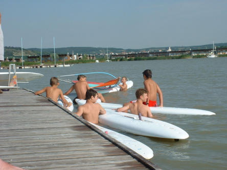 Foto zeigt Jungs mit Windsurfbrettern am Bootssteg