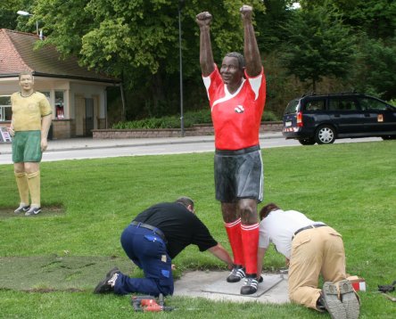 Zwei Mitarbeiter der Stadt helfen dem Fußballspieler auf die Beine: Nun ist die Mannschaft wieder komplett! © Dieter Retter 