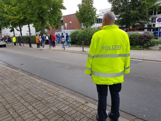 Auf dem Bild ist ein Polizist der Jugendverkehrsschule Kaiserslautern beim Kontrollieren des Verkehrs vor der Schule zu sehen. © Jugendverkehrsschule Kaiserslautern