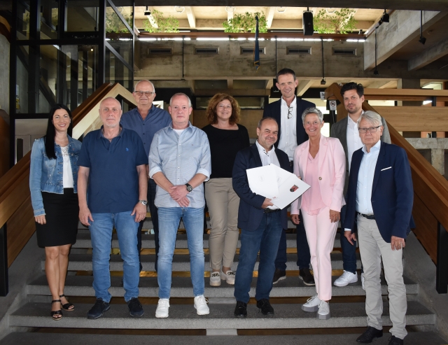 Klaus Hudomiet mit den drei Urkunden im Kreise seiner Kollegen, der zuständigen Referatsleitungen, des Personalrats und des Stadtvorstands auf der Treppe im Rathausfoyer. © Stadt Kaiserslautern