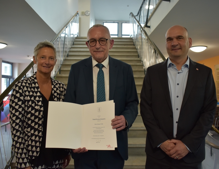 Rainer Wirth mit OB Beate Kimmel und Bürgermeister Manfred Schulz auf der Treppe im Rathaus Nord. Rainer Wirth hält seine Entlassungsurkunde in Händen. © Stadt Kaiserslautern