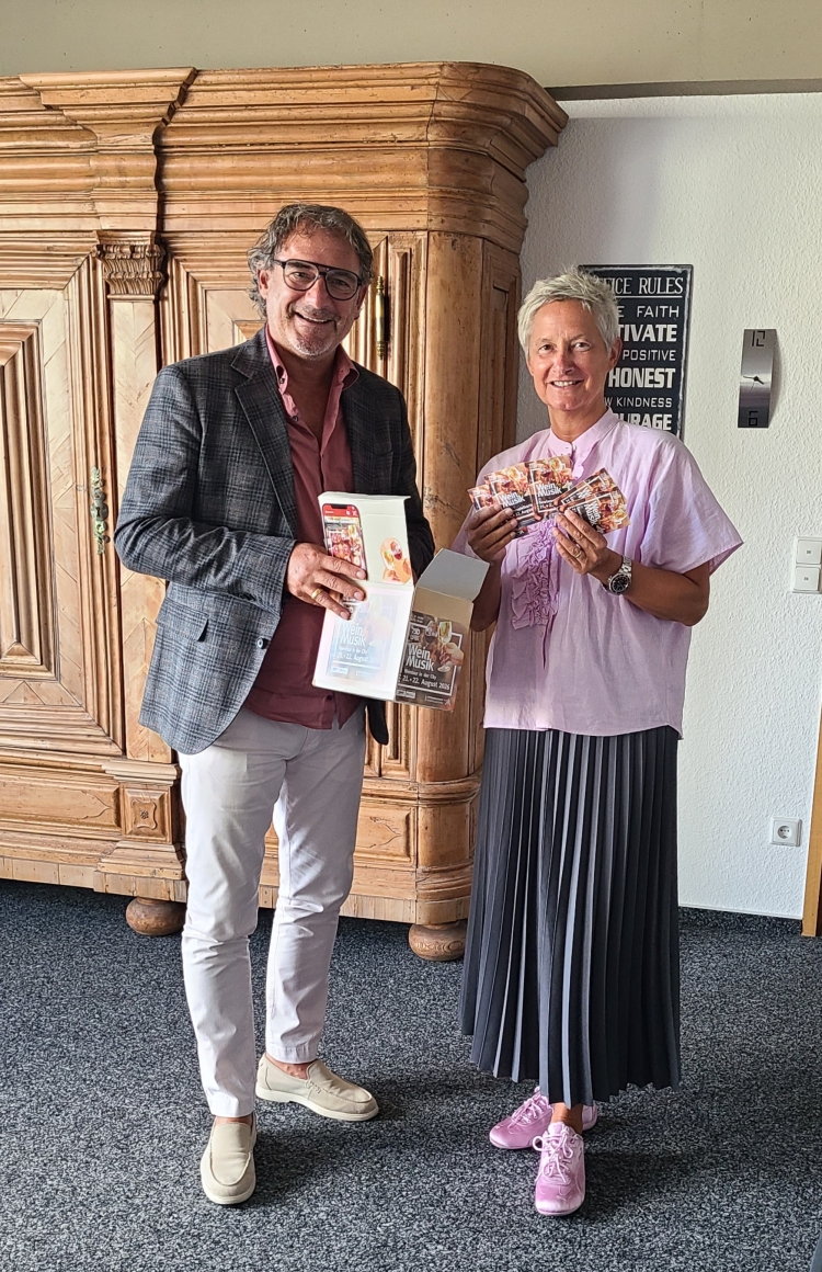 Alexander Heß und Beate Kimmel stehen im Dienstzimmer der Oberbürgermeisterin vor einem braunen Holzschrank. Alexander Heß hält die Kiste mit den Gewinnkarten, Beate Kimmel die gezogenen Gewinnkarten. © Stadt Kaiserslautern