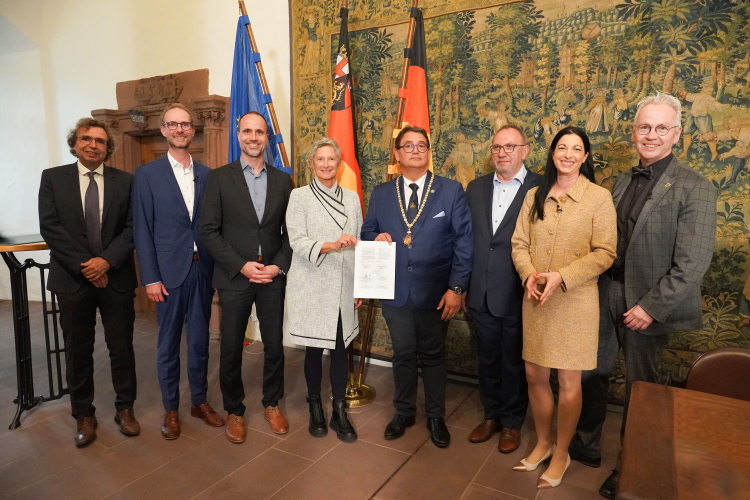 Die Anwesenden stehen mit dem frisch unterzeichneten Letter of Intent vor dem Wandteppich im Casimirschloss. © Westpfalz-Klinikum