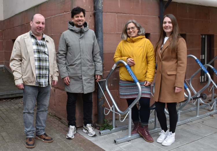 Umweltdezernent Manuel Steinbrenner (2.v.l.) mit der städtischen Radverkehrsbeauftragten Julia Bingeser (2.v.r.), Julia Merscher (1.v.r.) vom Referat Umweltschutz sowie Lothar Bendel (1.v.l.) als Vertreter des Burggymasiums bei der Anbringung der Aufkleber am Burggymnasium Kaiserslautern. © Stadt Kaiserslautern 	