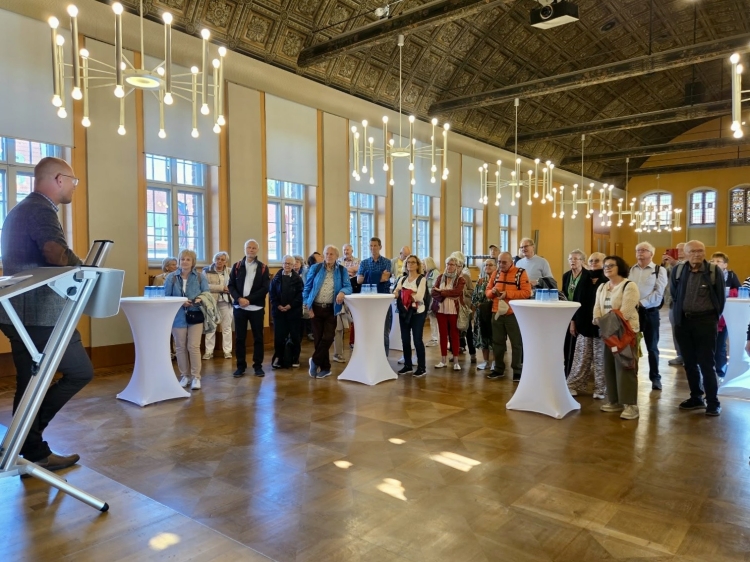Oberbürgermeister Daniel Keip  bei der Begrüßung der Gäste aus Kaiserslautern im Rathaus. Er ist von hinten fotografiert, mit Blick in den Raum auf die Gäste, die an Stehtischen stehen. © Stadt Brandenburg