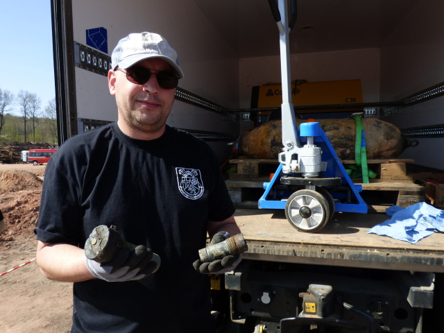 Peter Kappler mit Kopf- und Bodenzünder, dahinter die entschärfte Bombe, verschnürt zum Abtransport.  © Stadt Kaiserslautern