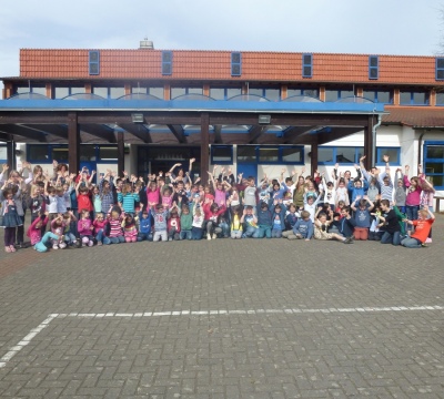 Gruppenfoto von winkenden Schülerinnen und Schüler der Grundschule Dansenberg vor dem Schulgebäude