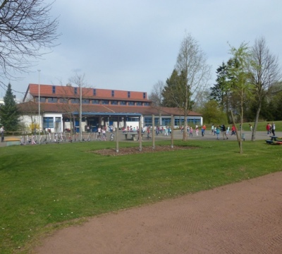 Schülerinnen und Schüler während der Pause im Schulhof. Im Hintergrund das Schulgebäude