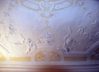 Die weiße Decke eines Ausstellungsraumes des Wadgasserhofs. Die weiße Decke besitzt viele Stuckelemente in Form von Putten, Vögeln, Pflanzen und Blumenreliefs.