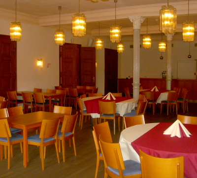 Im grünen Saal wurden mehrere Tische mit Bestuhlung aufgebaut. Durch die warmen, gelblichen Glaslampen und die kunstvollen, schlanken Säulen wird eine angenehme Atmosphäre geschaffen. 