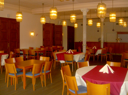 Im grünen Saal wurden mehrere Tische mit Bestuhlung aufgebaut. Durch die warmen, gelblichen Glaslampen und die kunstvollen, schlanken Säulen wird eine angenehme Atmosphäre geschaffen.  © Stadt Kaiserslautern