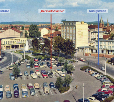 Eine Farbaufnahme des noch nicht existierenden Karstadtgeländes auf dem ein Parkplatz ist. Hinten ist das Pfalztheater zu sehen und davor ein Springbrunnen.