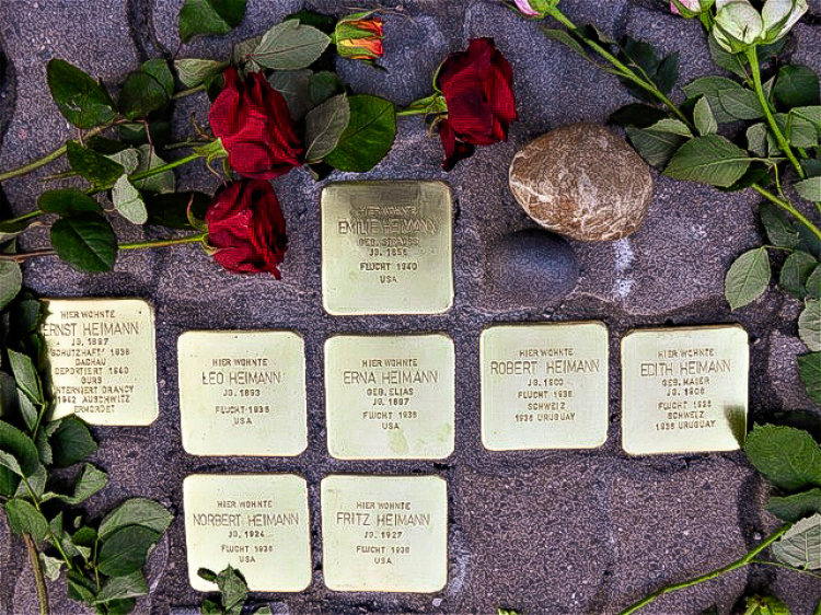 Auf dem Bild sieht man acht in den Boden eingelassene Stolpersteine. Rundherum liegen rote Rosen. © Georg Emme