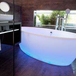 Die freistehende Badewanne besitzt eine ovale Form, die von unten blau erleuchtet wird.