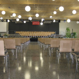 In the large event hall wooden chairs are assembled in series and show to the stage.